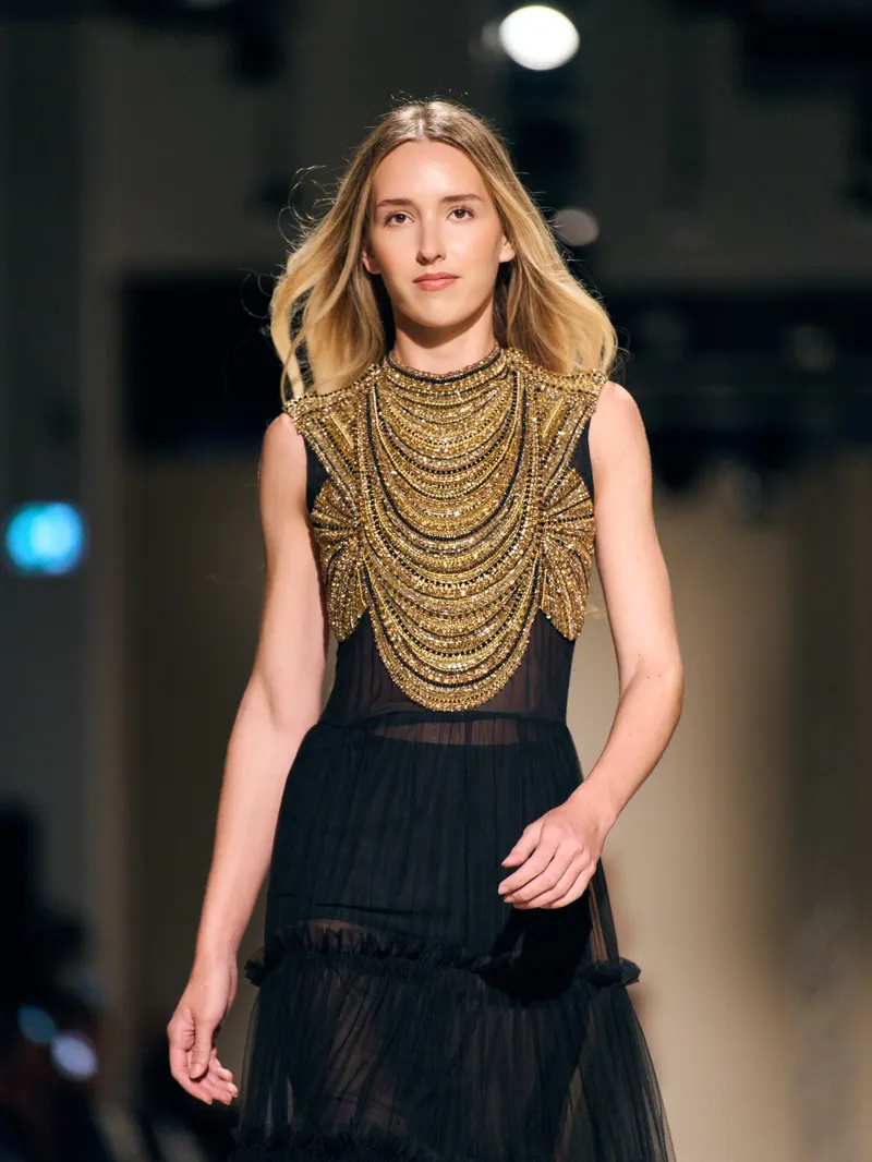 Lisa on the Dunesi runway in a black gown with a sculpted gold collar