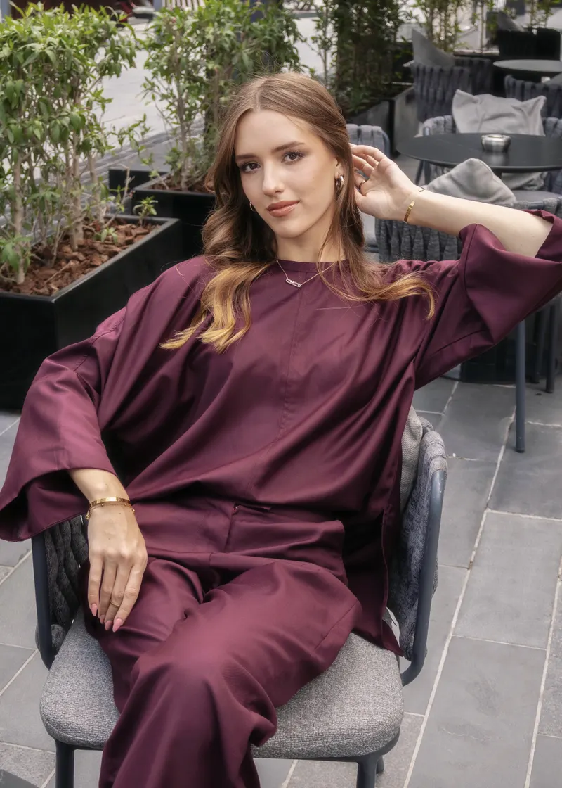 Lisa seated outdoors in a plum satin tunic and trousers