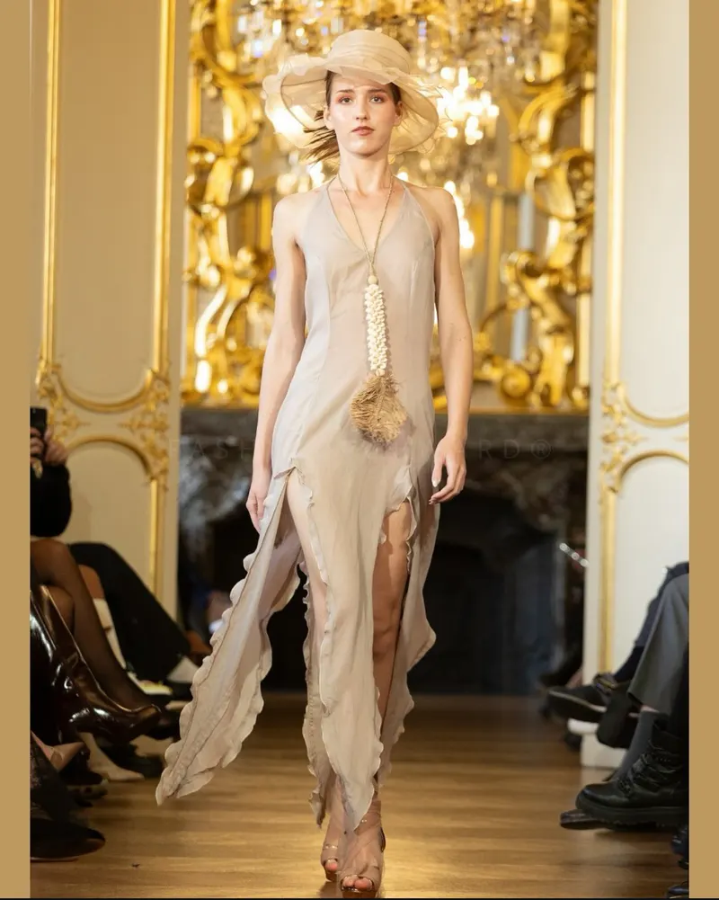 Lisa on a gilded salon runway in a sheer draped dress and hat